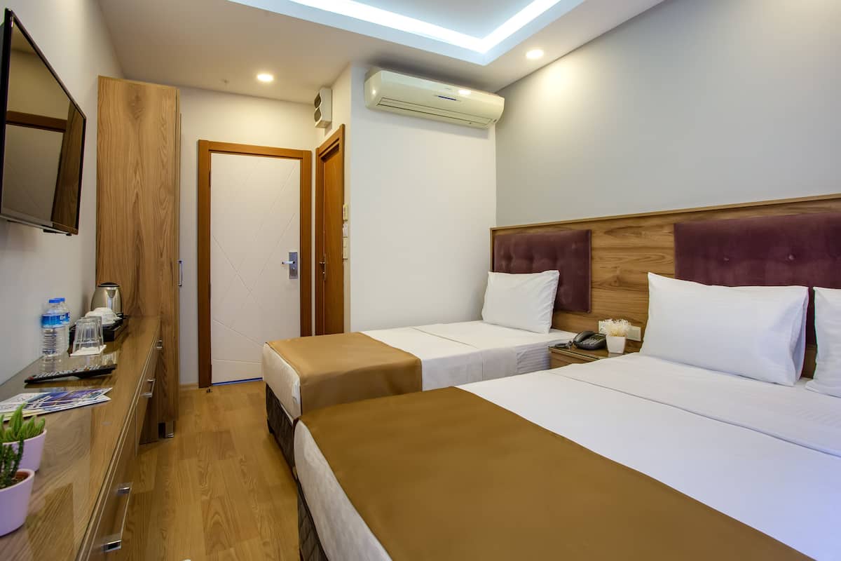 A hotel room with two beds, a wooden desk, a flat-screen TV, an air conditioning unit, and a door leading to another room.
