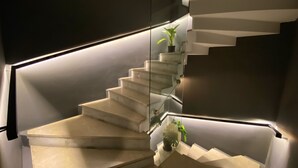 A modern spiral staircase with glass railings and integrated lighting, leading to a landing area with potted plants. - West Palace Hotel (Istanbul)