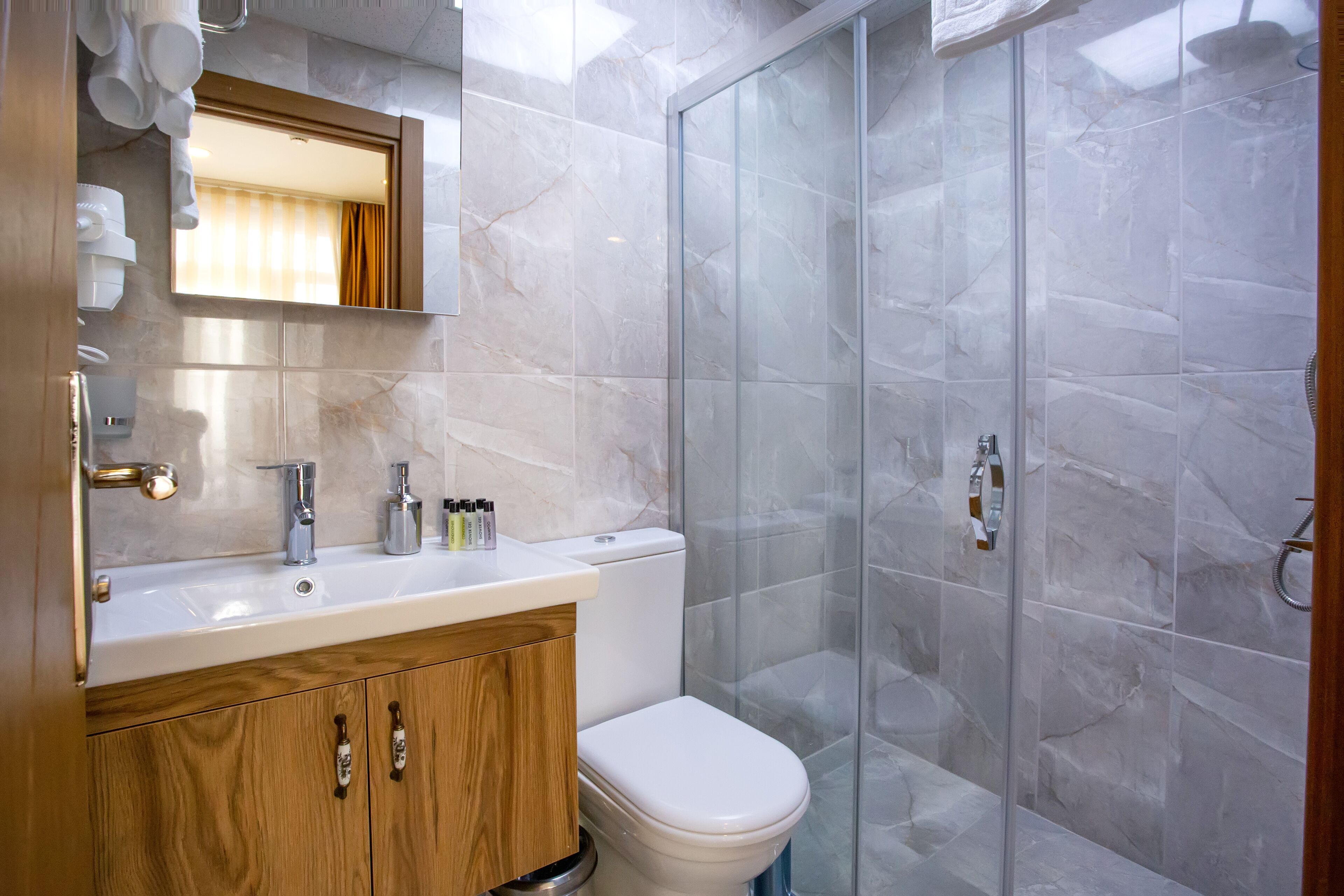 A modern bathroom with a marble sink, wooden cabinet, and a glass shower enclosure.