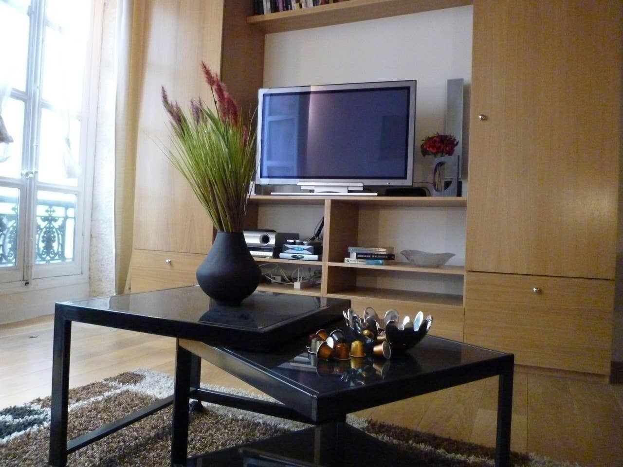 Ein Wohnzimmer mit Fernseher auf einer Holzkommode, einem schwarzen Couchtisch mit Dekoration und einem großen Fenster mit Aussicht.