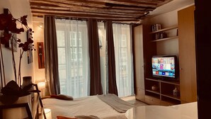 Une chambre à coucher avec un lit, une télévision, une bibliothèque et une fenêtre avec des rideaux.