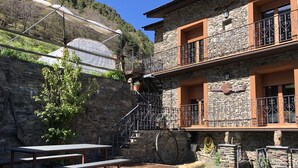 A stone building with a wooden deck, outdoor seating, and a staircase leading to a balcony. - Charming house in a quiet and rural environment HUT3 005/004 (Llorts)