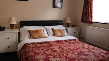 A bedroom with a bed, two nightstands, a lamp on each, a framed picture on the wall, and a window with curtains.