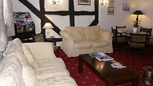 A cozy room with a red carpet, a sofa, a chair, a table with magazines, and a lamp. - The Croft (Bridgnorth)