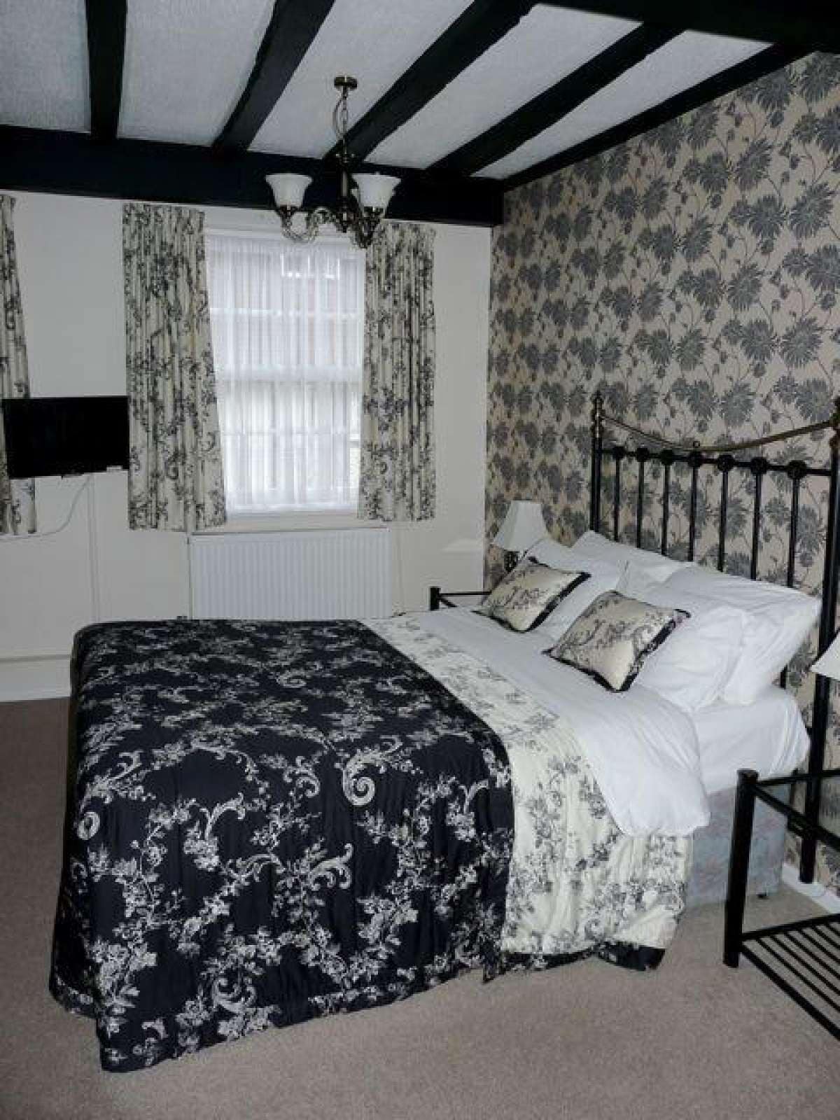 Un dormitorio con cama, candelabro, ventana con cortinas y papel tapiz estampado.