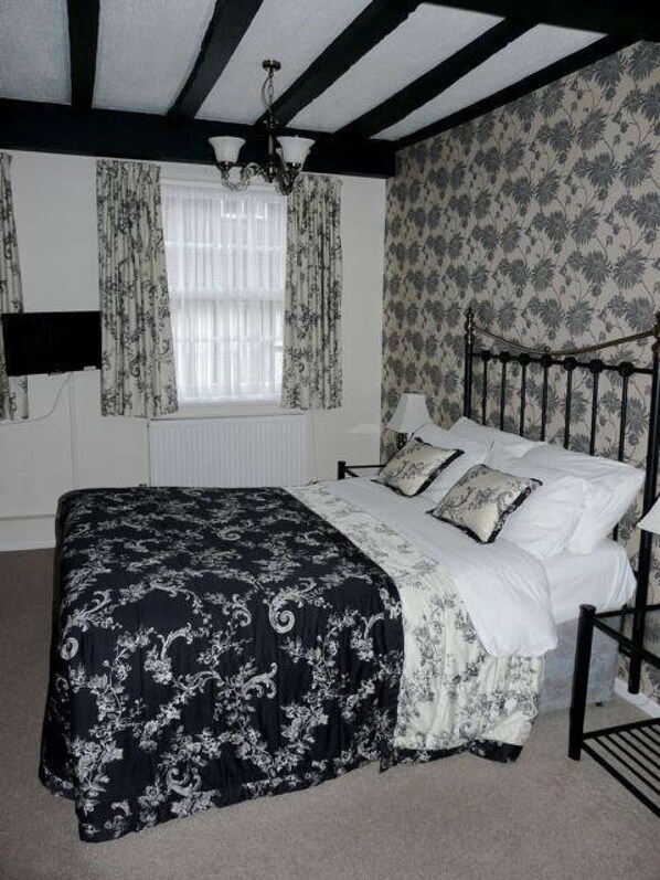 A bedroom with a bed, a chandelier, a window with curtains, and patterned wallpaper.
