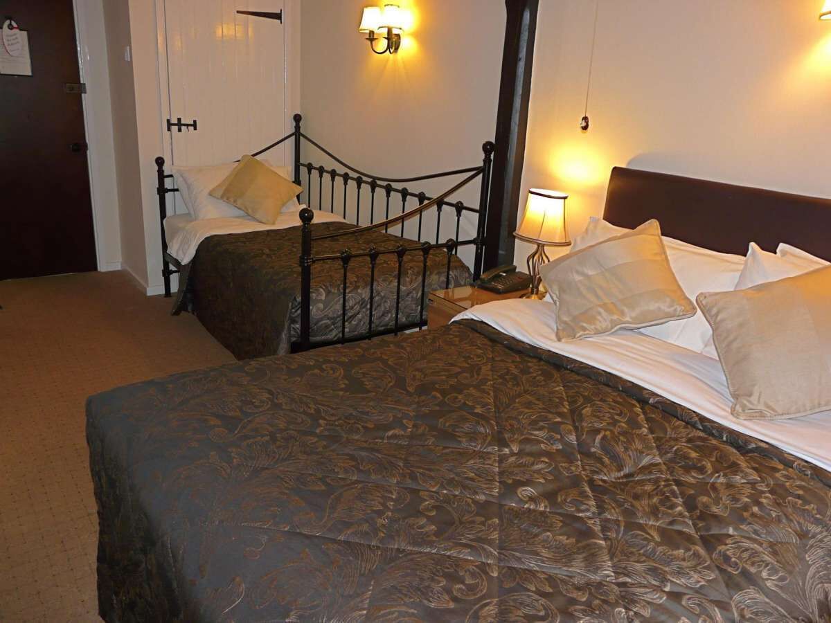 A hotel room with two beds, a dark metal headboard, a patterned bedspread, and wall-mounted lamps.