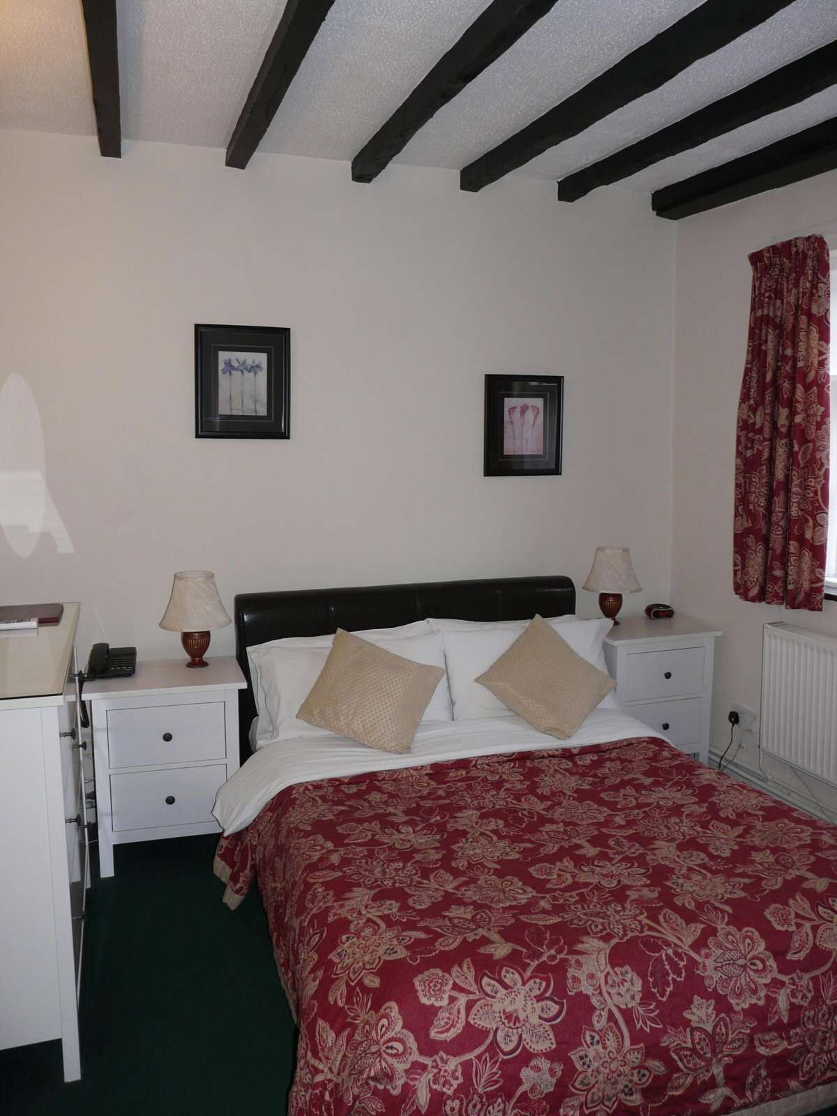 A bedroom with a bed, two bedside tables, a nightstand, a lamp, a framed picture, and a window with curtains.