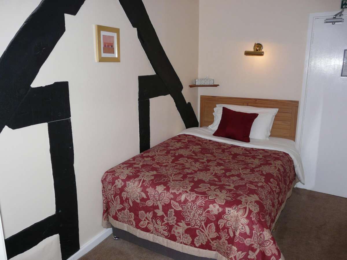 Un dormitorio con cama, cubrecama rojo y blanco con estampado floral, cabecera de madera, mesita de noche con lámpara y diseño en la pared en blanco y negro.