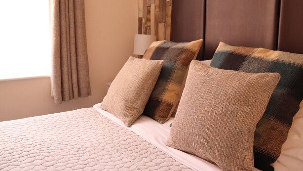 A neatly made bed with a quilted headboard, multiple pillows, and a lamp on a bedside table. - The Croft (Bridgnorth)