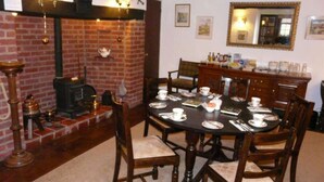A dining area with a brick fireplace, wooden chairs, a round table set for four, and a mirror on the wall. - The Croft (Bridgnorth)