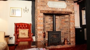 A cozy room with a brick fireplace, a red leather chair, and a sign that reads "Be our guest." - The Croft (Bridgnorth)