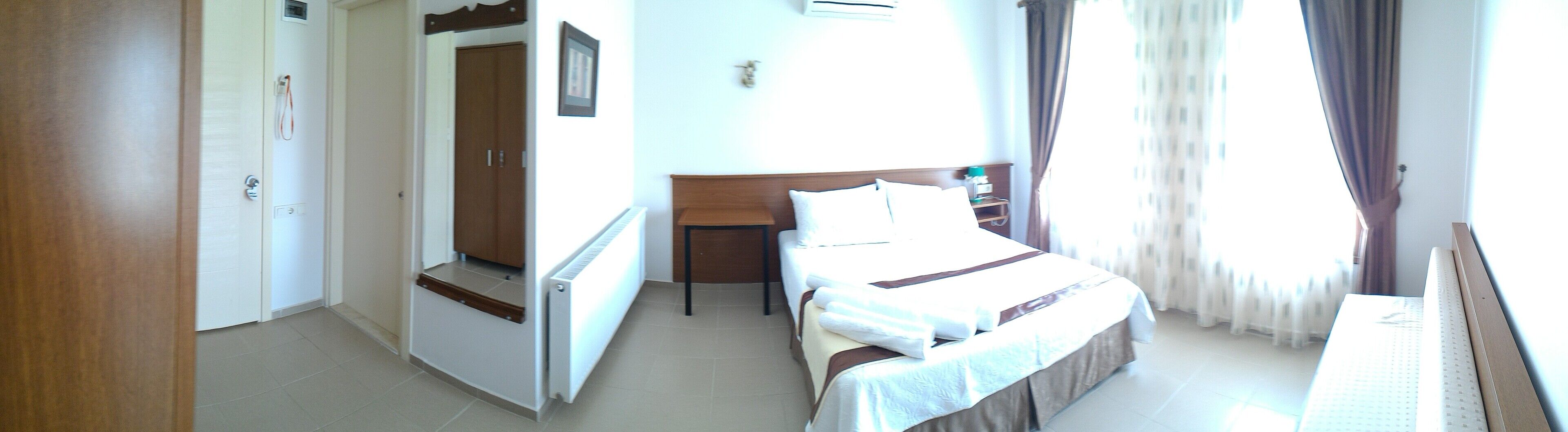 A hotel room with a bed, a desk, a radiator, and a window with curtains.