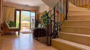 A hotel lobby with a staircase, a sofa, and a dining area visible through the glass doors. - Alibeyhan Otel (Ayvalik)