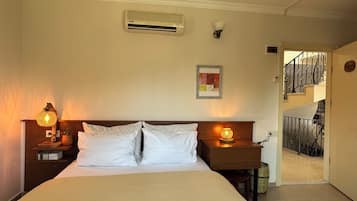 A bedroom with a bed, two bedside tables, a wall-mounted air conditioner, a framed picture, and a staircase leading to an upper floor.