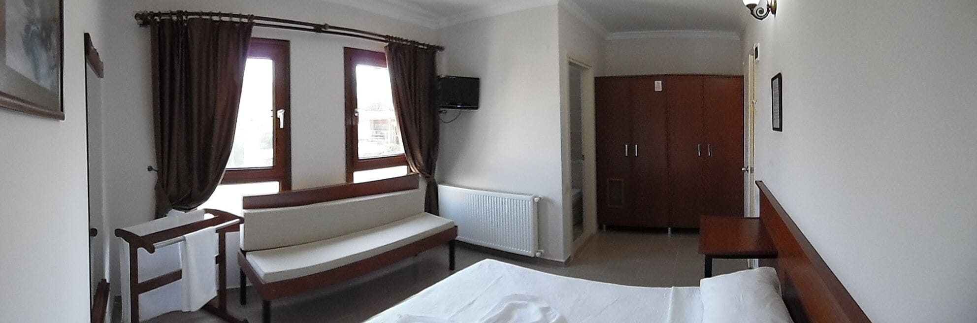 A hotel room with a bed, a bench, a TV, a wardrobe, and a window with curtains.