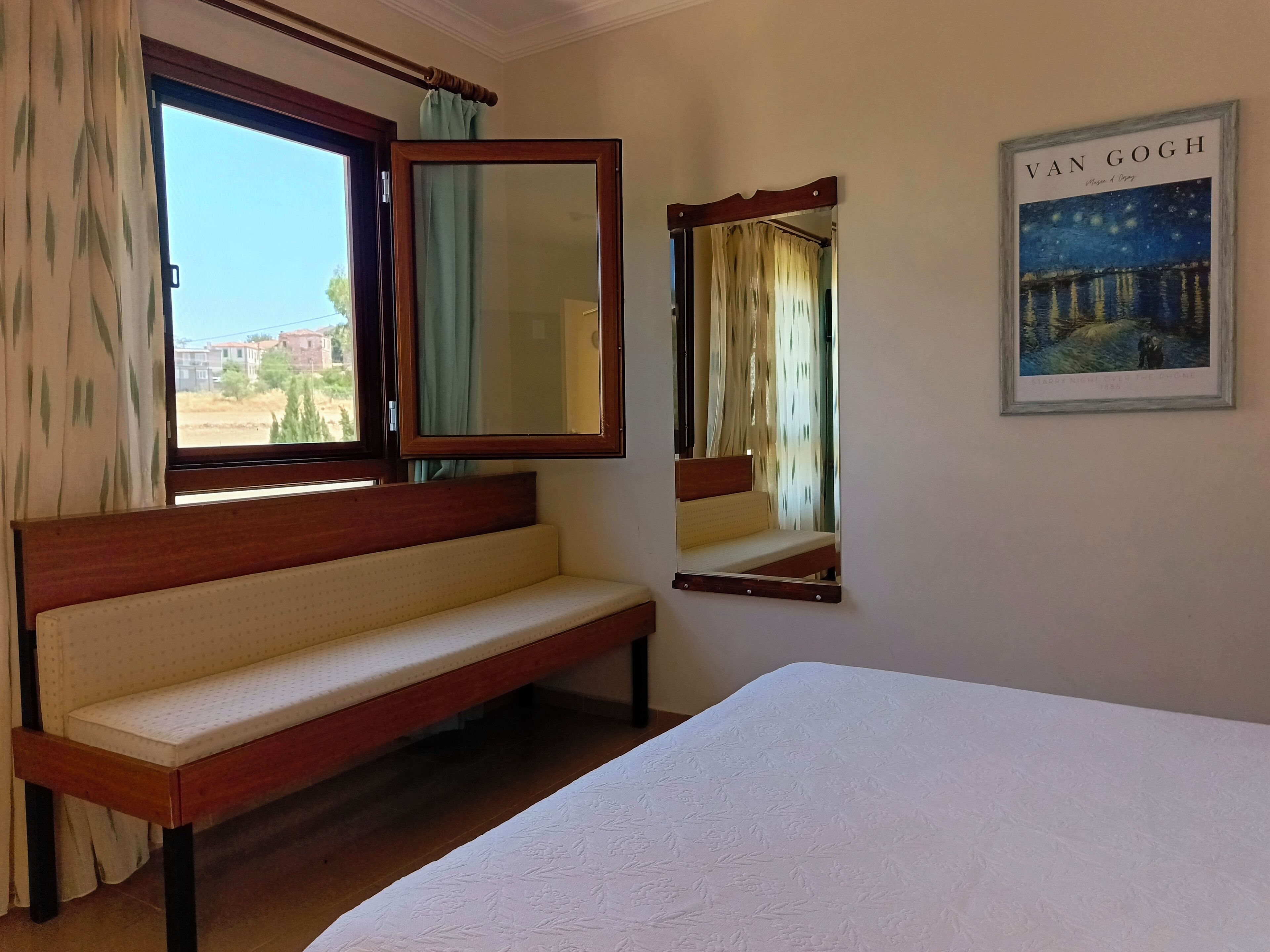 Habitación de hotel con cama, banqueta, espejo grande y pintura de 'La noche estrellada' de Van Gogh.