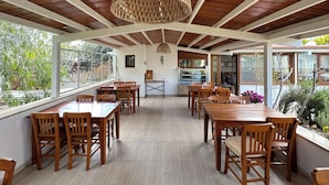 A spacious dining area with wooden tables and chairs, a large woven pendant light, and a view of the outdoors through large windows. - Alibeyhan Otel (Ayvalik)
