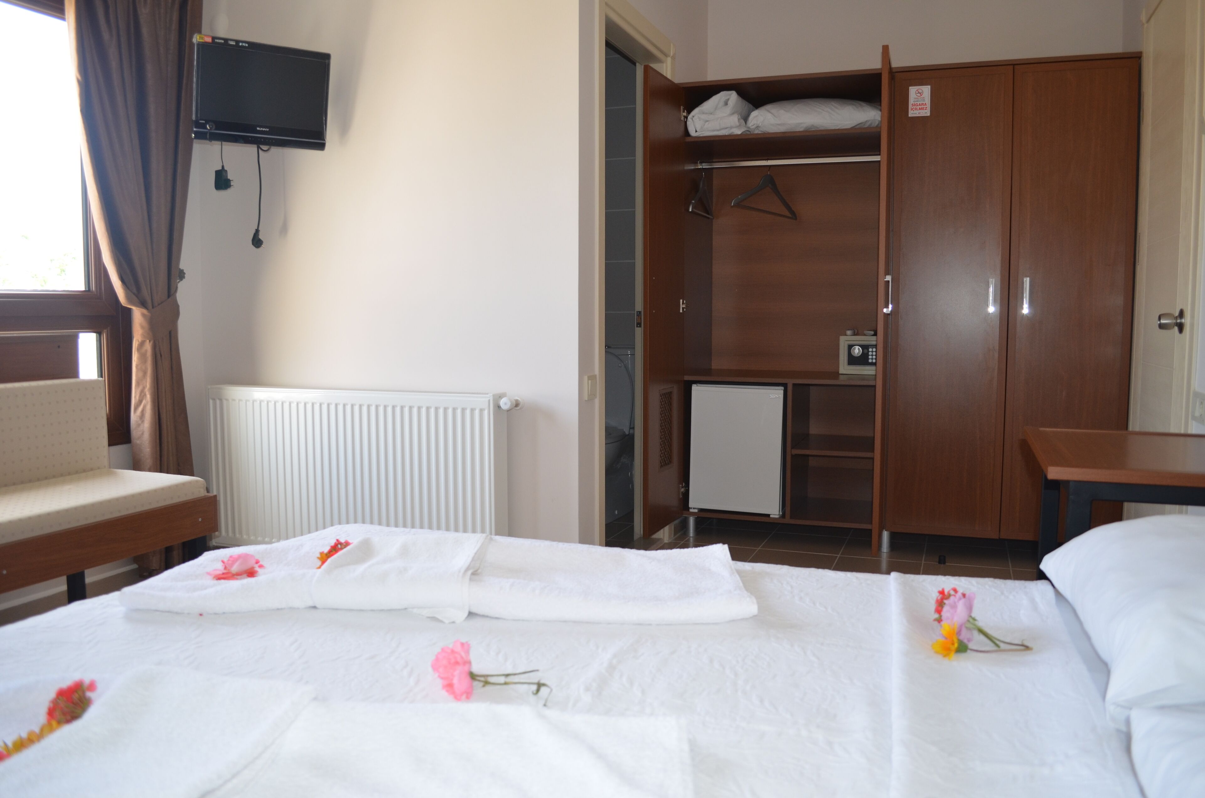 Habitación de hotel con cama, televisor montado en la pared, armario y radiador.