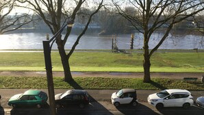 A parking lot with several cars parked along the side of a road. There are trees and a grassy area with a body of water in the background. - Gästeträume (Bremen)