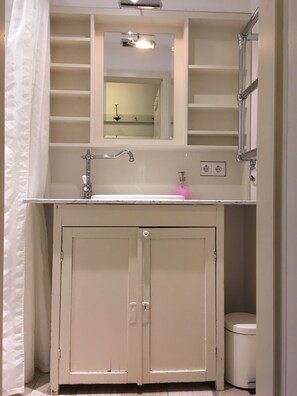 A bathroom with a white sink, mirror, and cabinet. There is a shower curtain, a toilet, and a trash can.