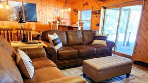 A cozy cabin interior with a large leather sofa, a matching ottoman, and a wooden floor.