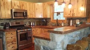 A kitchen with wooden cabinets, a stone island, a microwave, and a stove.