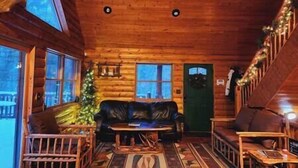 A cozy cabin interior with a wooden ceiling, a sofa, a coffee table, and a Christmas tree.