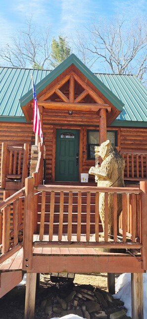 A wooden cabin with a green roof, a front door, and a porch with a lion statue. - Black Bear Cabin-Hot tub, Pet friendly, Riverfront (Baldwin)
