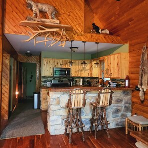 A rustic kitchen with wooden cabinets, a stone island, and a ceiling-mounted animal skull. - Black Bear Cabin-Hot tub, Pet friendly, Riverfront (Baldwin)