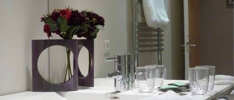 A bathroom with a white sink, a mirror with a circular frame, a towel rack, and a vase with flowers.