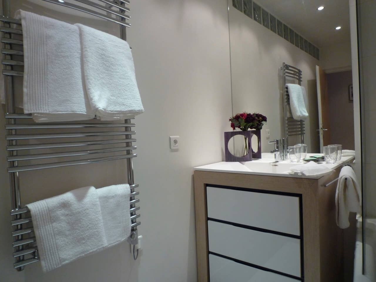 Ein modernes Badezimmer mit Handtuchhalter, Spiegel und Waschbecken mit Blumen in einer Vase.