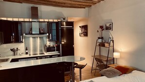 Une cuisine compacte dotée d’appareils électroménagers modernes, un coin repas avec une petite table et des chaises, et un lit avec des oreillers.