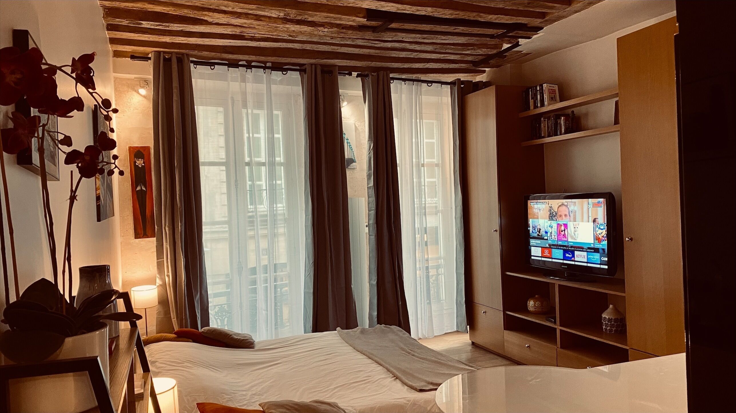 Una camera da letto con un letto, una televisione, una libreria e una finestra con tende.
