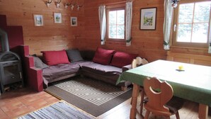 A cozy cabin interior with a wooden floor, a sofa with red cushions, a table with a green tablecloth, and a fireplace. - Preberhütte in Prebertal lies at 1500 meters above sea level (Tamsweg)