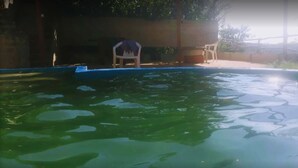Una piscina con agua cristalina y algunos objetos flotando. Hay dos sillas y una mesa cerca de la piscina.