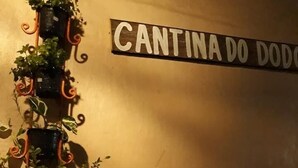 Una mesa con mantel a cuadros, una copa de vino tinto y un menú. Hay plantas en macetas sobre una estantería de pared.