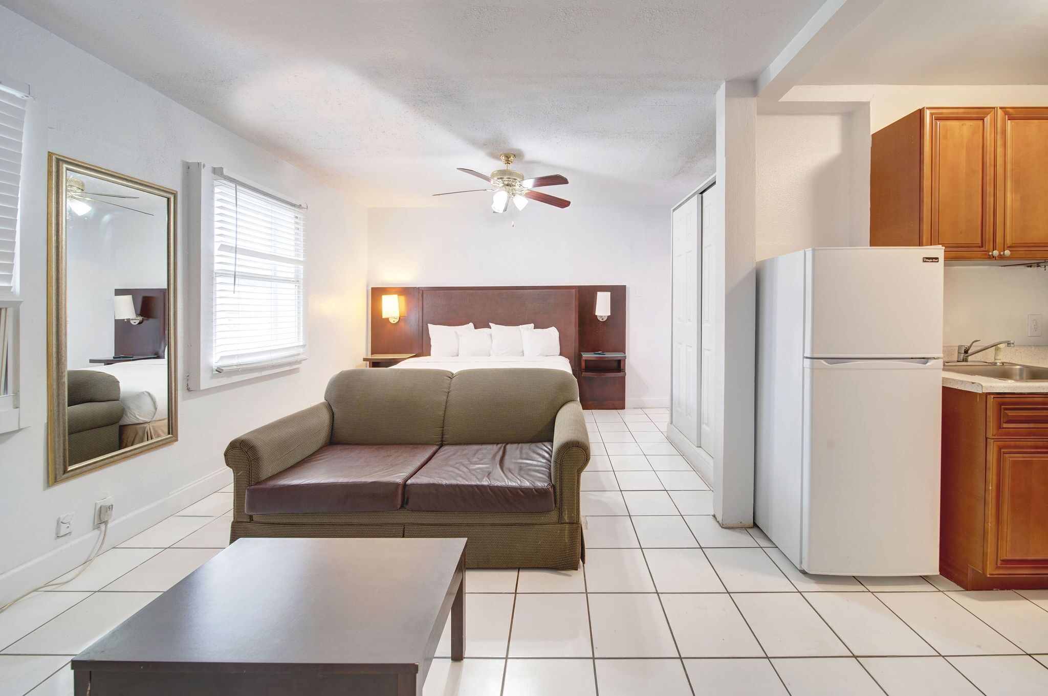 Habitación de hotel compacta con kitchenette, una cama, un sofá, una mesa de comedor y un ventilador de techo.