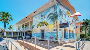 Um edifício com um mural de uma cena de praia, uma placa indicando quarto disponível e uma bandeira.