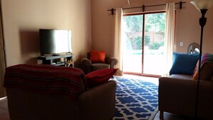 A hotel room with a bed, a sofa, a TV, and a large window with a view of greenery.