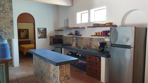 A kitchen with a central island, a refrigerator, a microwave, and a stove. There are two windows and a tiled backsplash.
