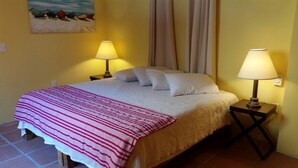 A neatly made bed with a striped blanket, two bedside lamps, and a painting of boats on the wall.