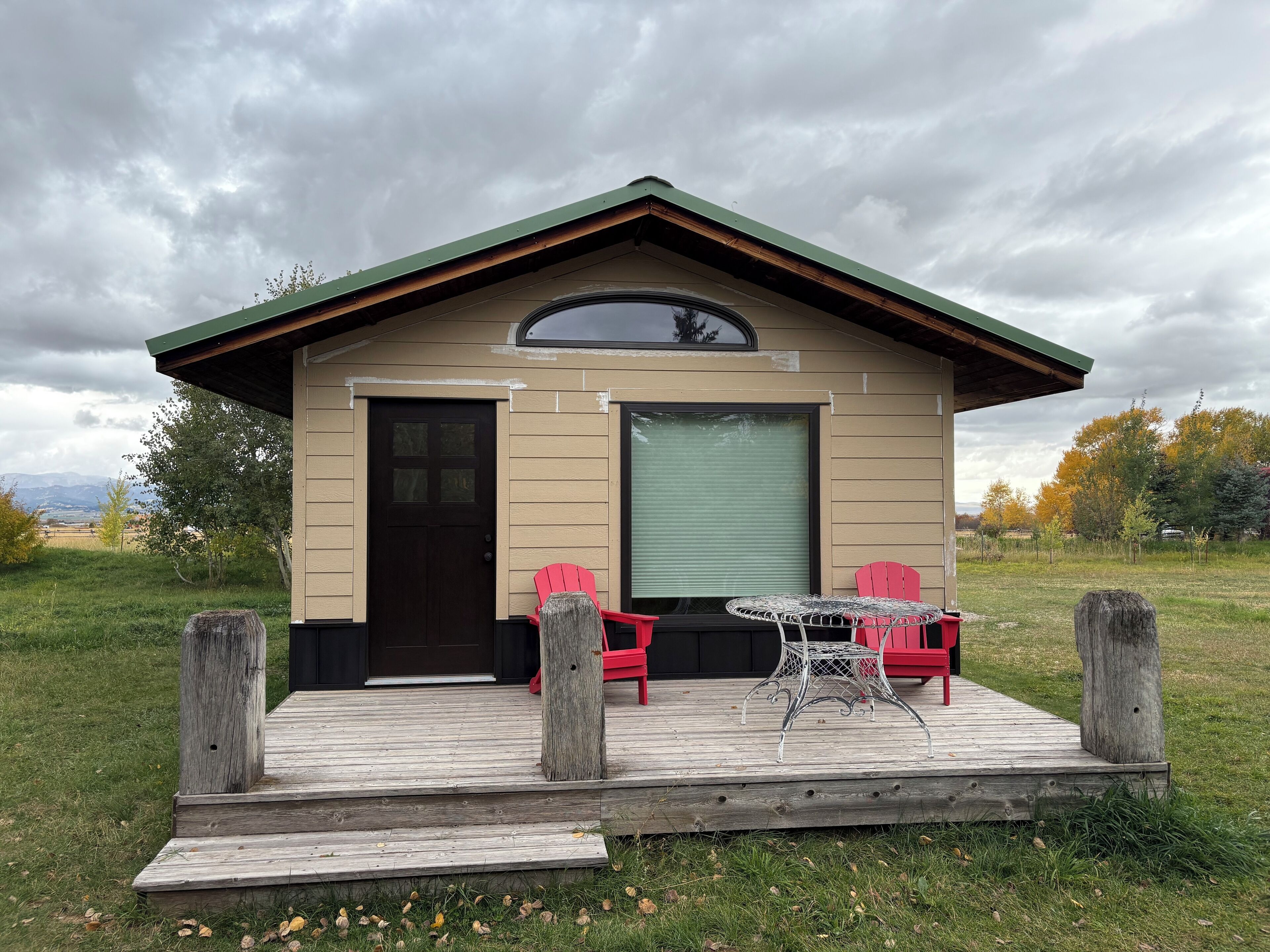 Een klein huis met een veranda, een deur en twee rode stoelen.