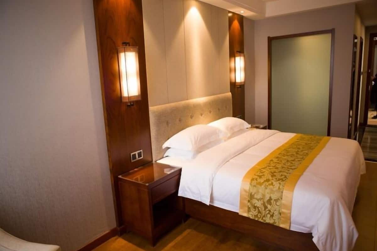 A hotel room with a large bed, wooden headboard, bedside lamps, and a wooden nightstand.