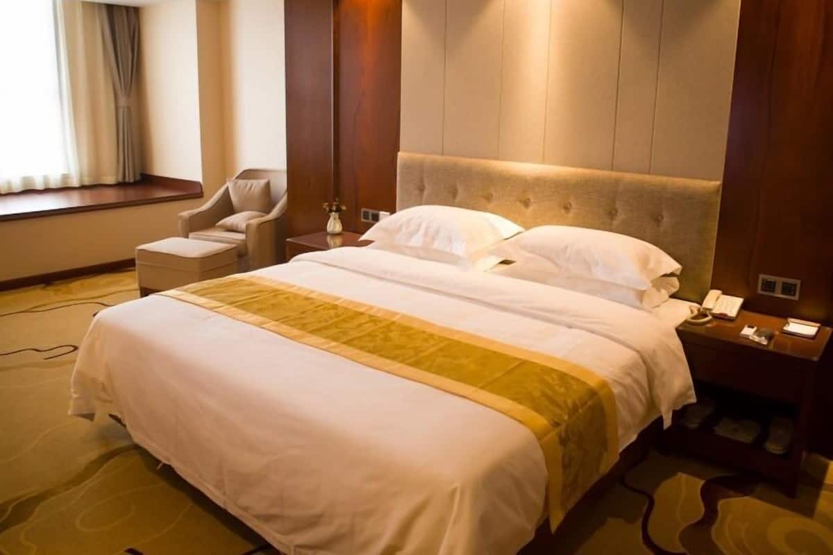 A hotel room with a large bed, a chair, a bedside table, and a window with curtains.