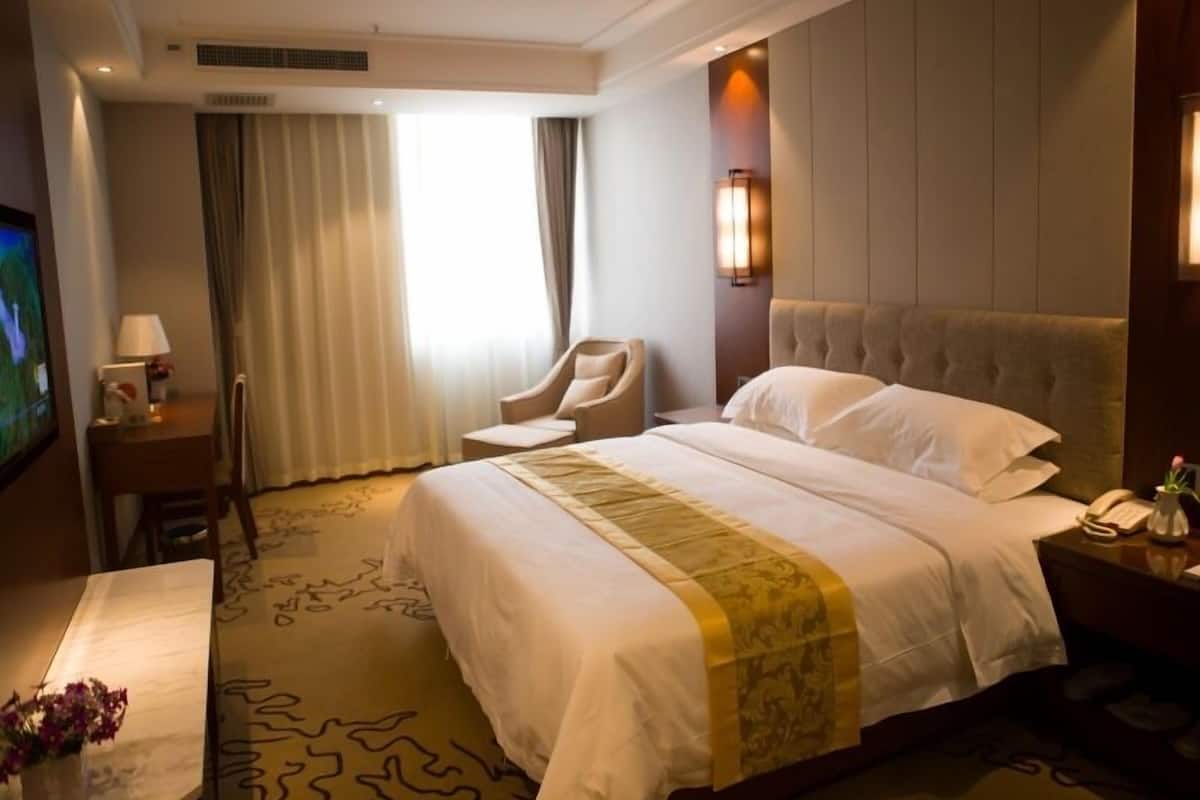 A hotel room with a large bed, a chair, a desk, and a TV.