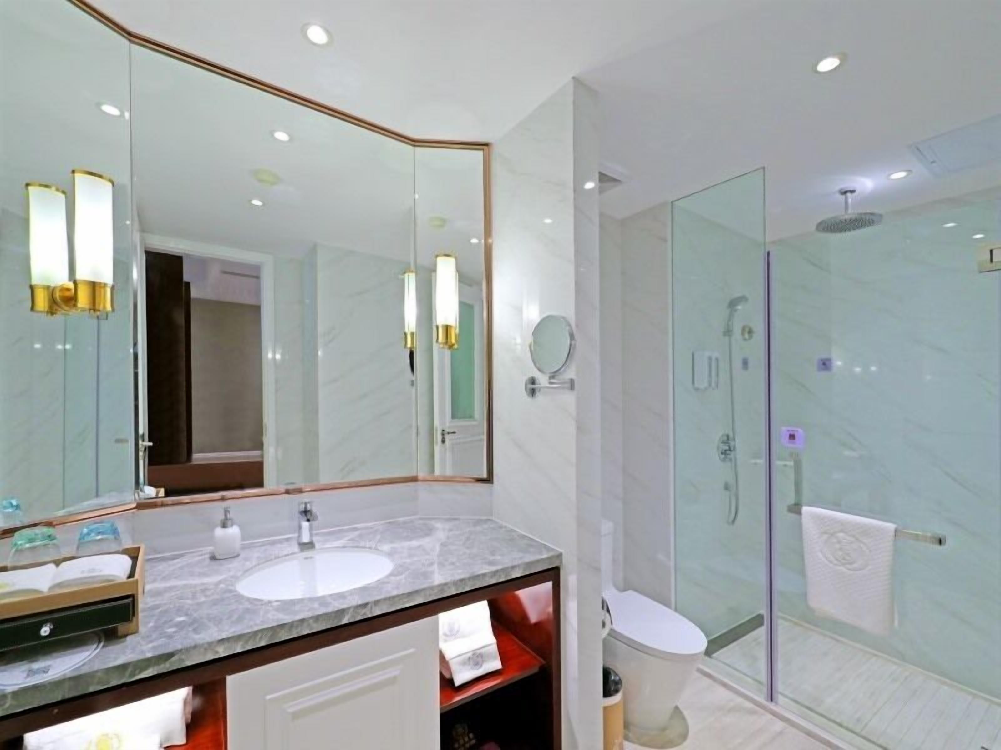 A modern bathroom with a marble sink, a large mirror, and a glass-enclosed shower.