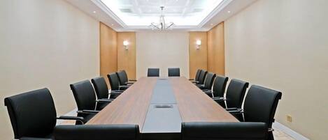 A conference room with a long wooden table, black chairs, and a modern chandelier.