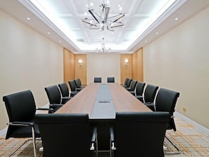 A conference room with a long wooden table, black chairs, and a modern chandelier.