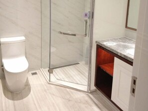 Et moderne badeværelse med glasvæg omkring brusebad, et hvidt toilet og en bordplade i marmor.